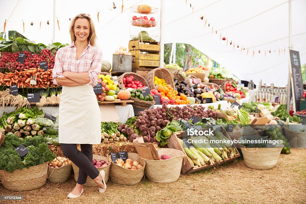 Large fresh food market with employee Female Stall Holder At Farmers Fresh Food Market, Strading And Smiling To Camera Farmer's Market Stock Photo