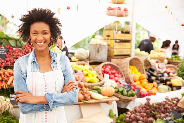 Female Stall Holder At Farmers Fresh Food Market Female Stall Holder At Farmers Fresh Food Market, Smiling To Camera vegetable stand stock pictures, royalty-free photos & images