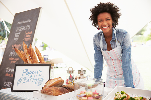 Female Bakery Stall Holder At Farmers Fresh Food Market, Smiling To Camera