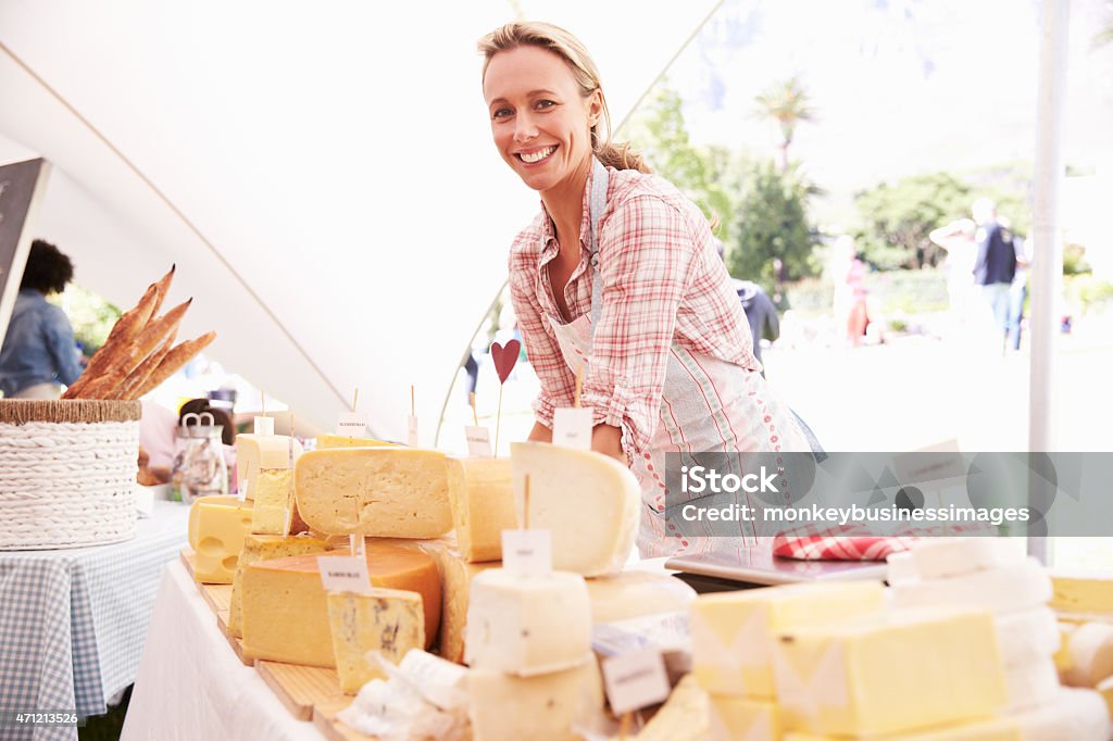 Smiling young woman at market display of fresh cheese Woman Selling Fresh Cheese At Farmers Food Markett, Smiling To Camera Cheese Stock Photo