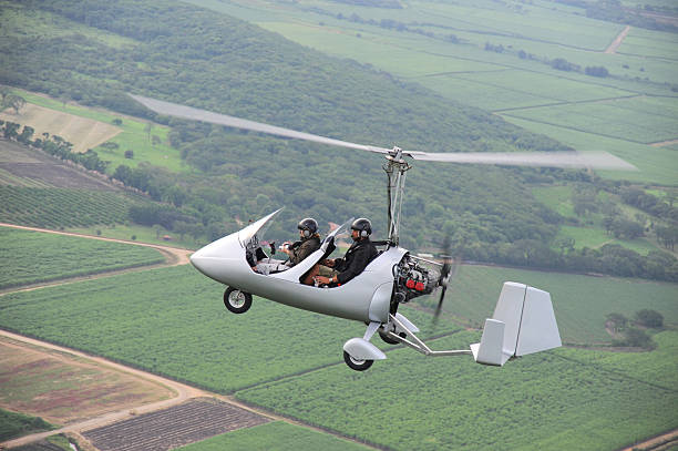 An autogyro flying over a green farmland Autogyro flying over the tropical landscape ultralight photos stock pictures, royalty-free photos & images