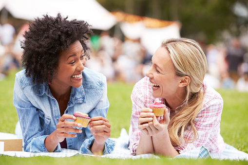Two Female Friends Enjoying Cupcakes At Outdoor Summer Event, Laughing