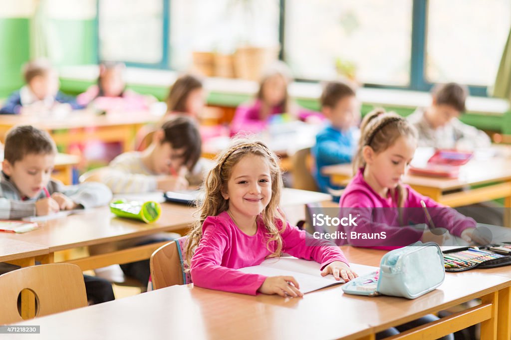 Group of elementary students in the classroom. Large group of children in a classroom. Focus is on smiling schoolgirl looking at the camera. 2015 Stock Photo