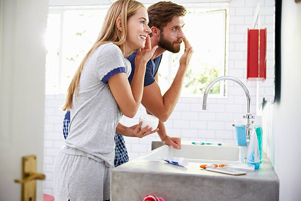 Couple In Pajamas Putting On Moisturizer In Bathroom