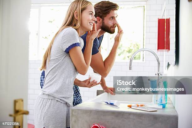 Couple In Pajamas Putting On Moisturizer In Bathroom Stock Photo - Download Image Now