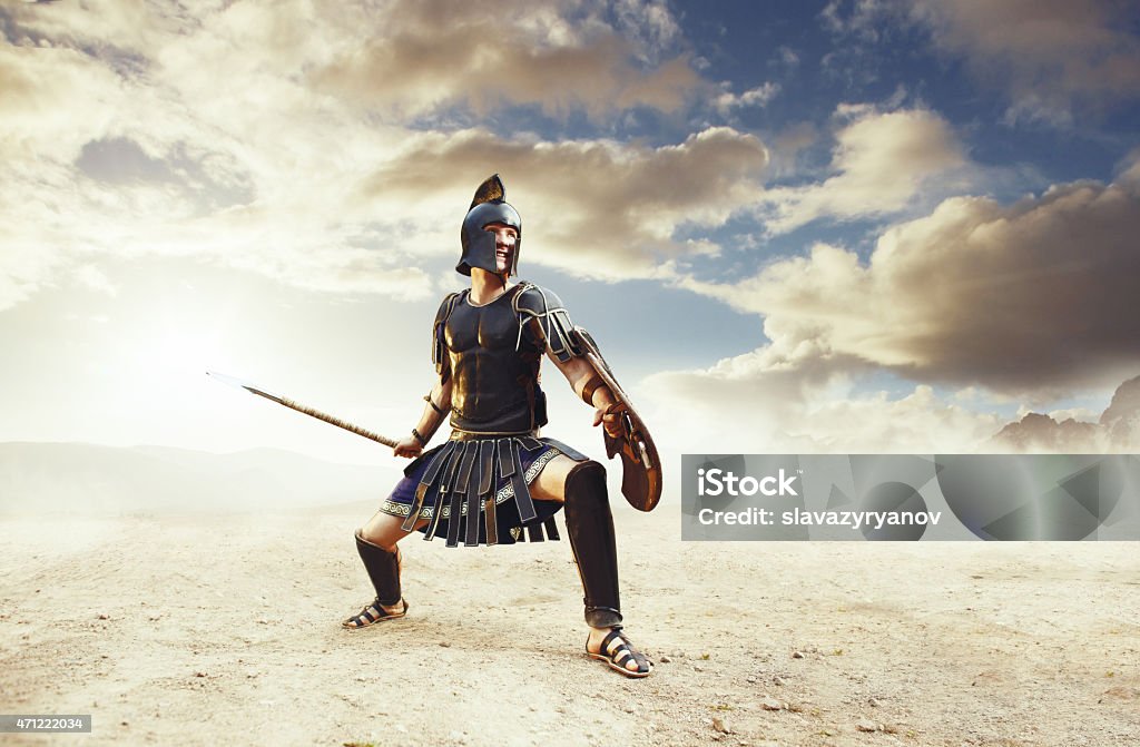 Ancient warrior in a typical black costume holding a spear Ancient Greek rome warriors fighting with swords and shields in the combat on sand and dust. Achilles and Hector fighting at Troy Gladiator Stock Photo
