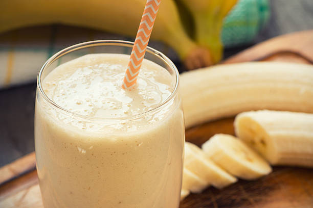 Fresh-made glass of banana smoothie with straw on wood stock photo