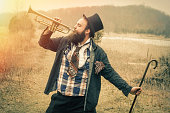 A gypsy holding a cane playing the trumpet