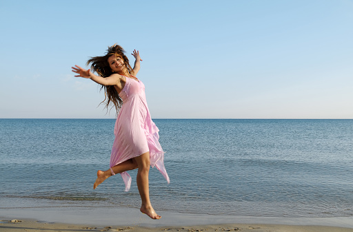 Young woman with pink dress jumping on the water's edge