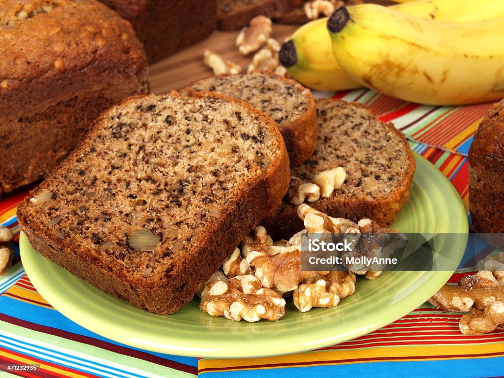 Banana Bread Slices with Walnuts and Bananas Banana bread sliced setting on a plate with whole walnuts with bananas and bread loaf in background Banana Stock Photo