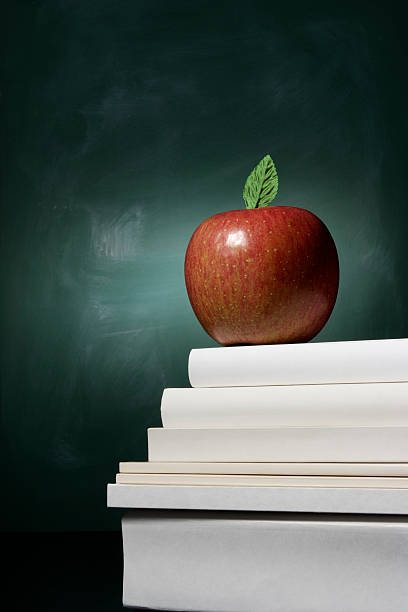 Red apple on stacked blank books in front of blackboard