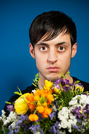 Puzzled young man holding bouquet of flowers.