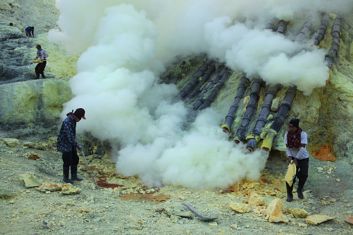 Kawah Ijen, Indonesia - August 8, 2011: Miners collect sulphur in the fumes of toxic volcanic gas at the sulphur mines in the crater of the active volcano of Kawah Ijen, East Java, Indonesia.