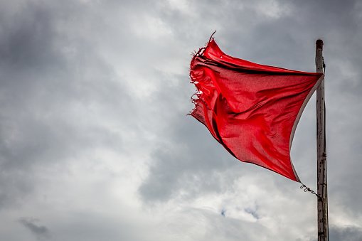 A wind torn red warning flag indicating danger on an English beach.