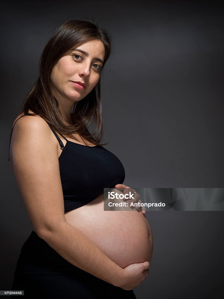 Pregnant woman A pregnant woman holds her big belly over a gray background. Achievement Stock Photo