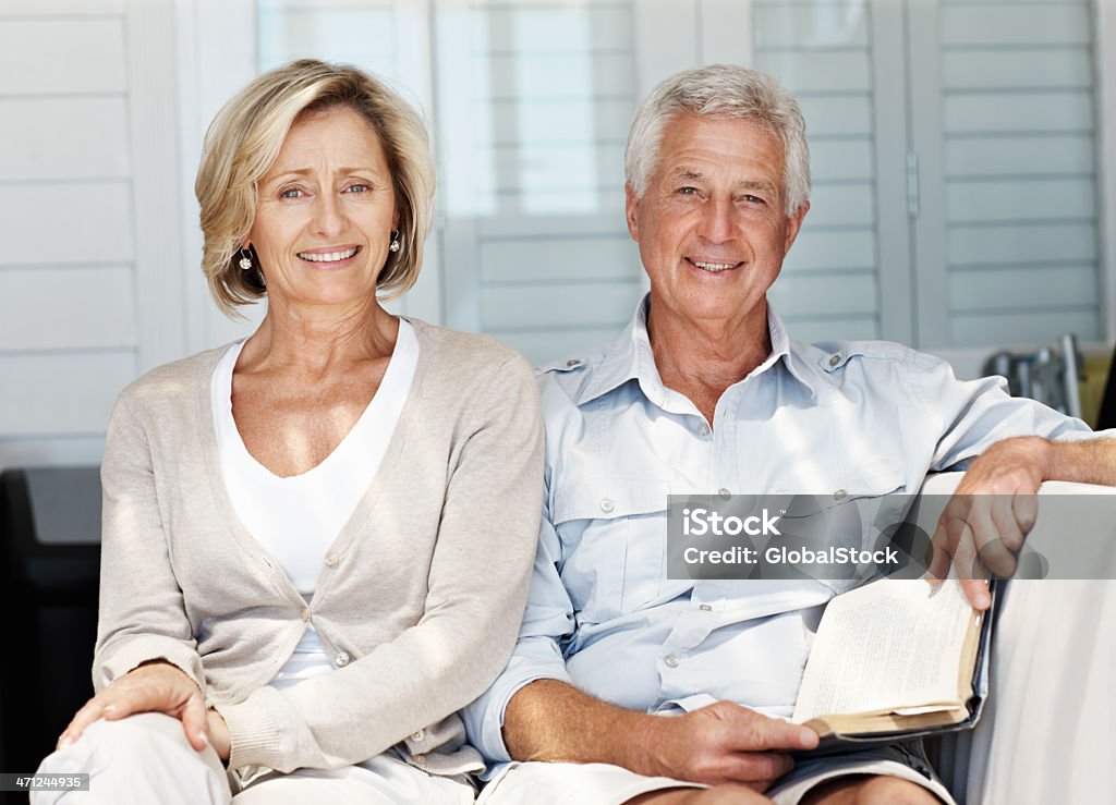 Bell'uomo maturo lettura libro con la moglie su un divano - Foto stock royalty-free di 50-54 anni