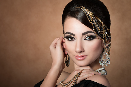 Portrait of young beautiful asian woman with evening make-up wearing head accessories and touching her face over beige background