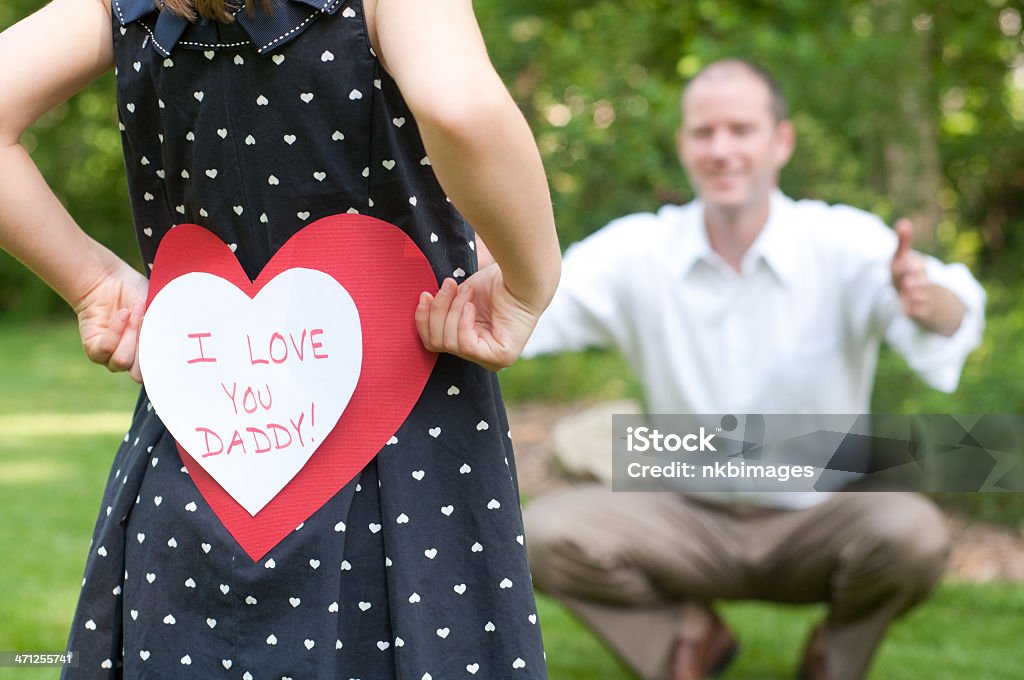 Girl with I love you daddy card for her father Girl in heart dress holds "I Love You Daddy!" card behind her back for her Dad.Related images:  Adult Stock Photo