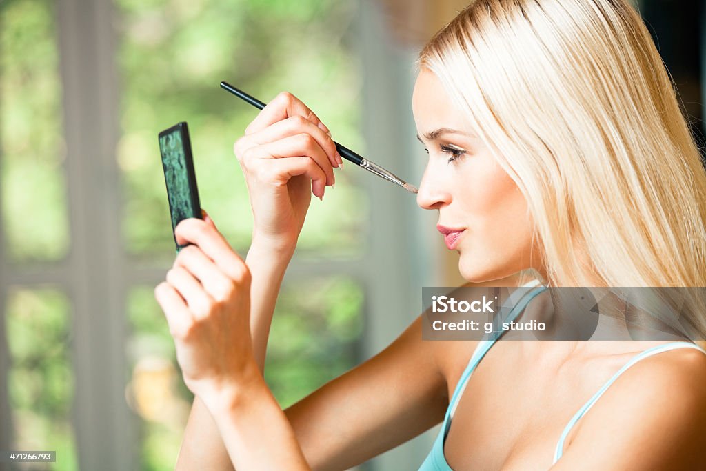 Portrait of smiling beautiful young woman with makeup brush indoors Adult Stock Photo