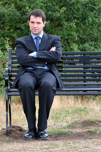 Businessman sitting on park bench, with his arms crossed and looking straight at the camera.