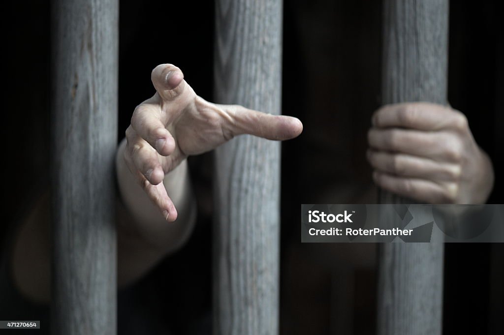 A person behind bars in prison  prisoner behind wooden bars Prison Stock Photo