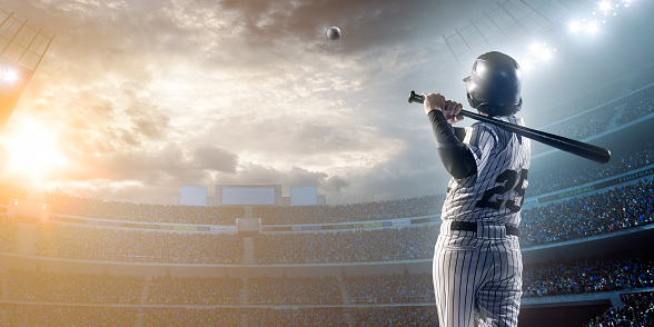 A male baseballs batter makes a dramatic play by hitting a ball.  The stadium is blurred behind him. Only the lights of the stadium shine brightly, creating a halo effect around the bulbs.