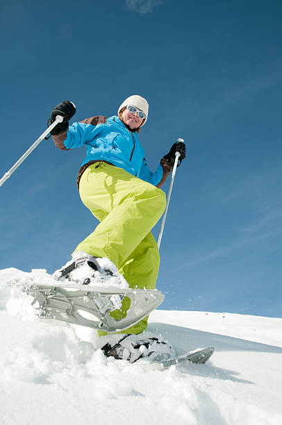 Standing on snowy ledge, woman dressed in vivid winter clothing is taking a photograph with her smartphone, overlooking a deep gorge blanketed in snow with a free copy space.