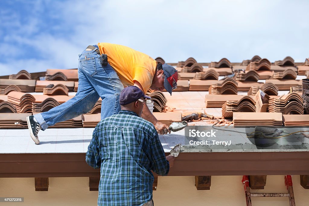 Dirty Jobs Two roofers applying "mud" (concrete) to set clay roof tiles. New Stock Photo