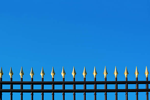 istock Old metallic fence with gold tips on blue background 471276328