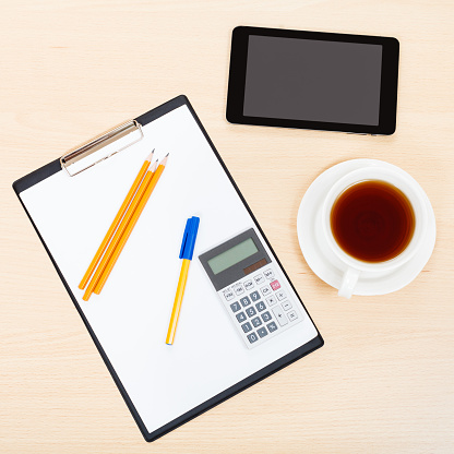 business still life - top view of tablet PC, clipboard, calculator, cup of tea, pen and pencil on office table