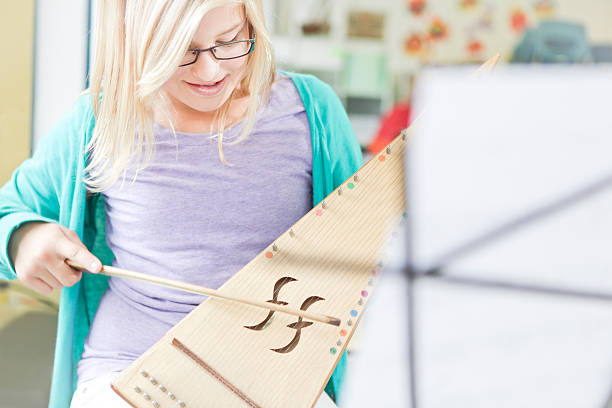 Girl Learning to Play an Instrument Girl in music class learning to play a bowed psaltery, a type of harp/zither.Music stand with sheet music blurred in the foreground. psaltery stock pictures, royalty-free photos & images