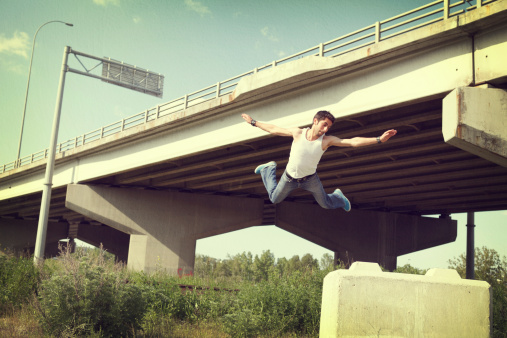 young man leaping off large cement block twisting in the air during a parkour run - Processed with texture added for a retro feel.