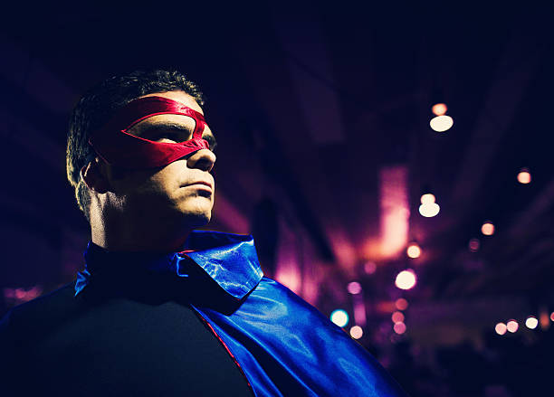 man with blue cape and red mask posing like a superhero under what appears to be a bridge, using LED lights.