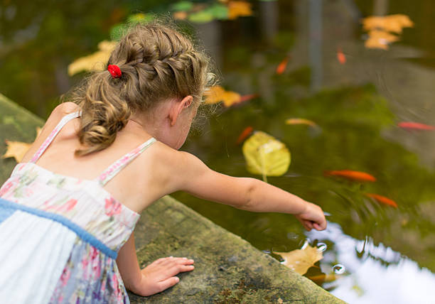 Little girl sitting by the pond with fish.