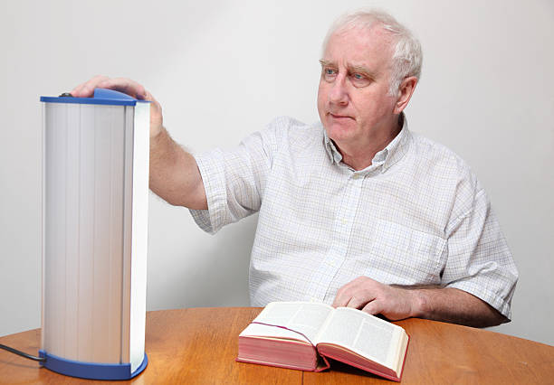 senior man adjusts seasonal affective disorder SAD lamp senior man adjusts seasonal affective disorder SAD lamp - these lamps simulate strong daylight and are believed to be effective i controlling  depression associated with lack of daylight in winter months -  "Seasonal Affective Disorder" or SAD light therapy stock pictures, royalty-free photos & images