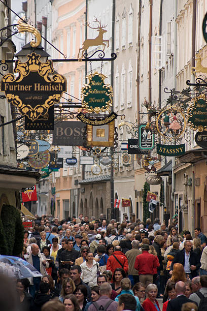 Salzburg, Austria - May 22, 2010: Tourists crowd the historical Getreidegasse street where Mozart was born in 1756. Getreidegasse is also famous for its wrought-iron store-front signs, that remind of earlier times before literacy was common among the people. Many tourists visit Salzburg in the summer time to enjoy the well-preserved European traditional culture. Shallow DOF with main focus at center of image.