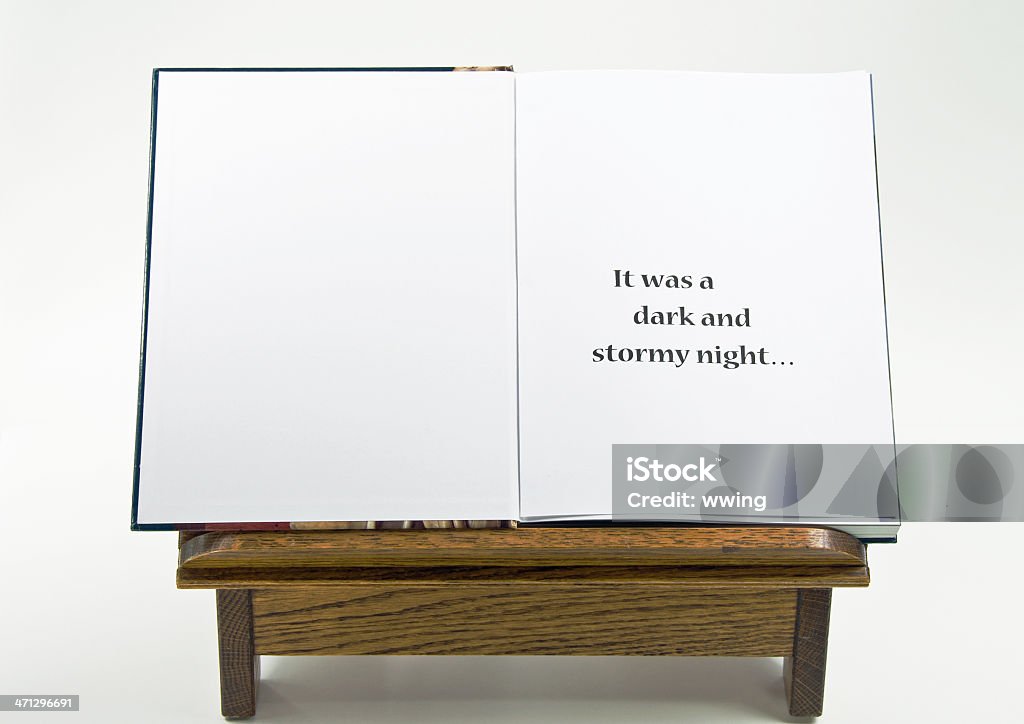 Open  Book with Cliche An open book with one page showing the words "it was a dark a stormy night" and a page for copy space. It is resting upon an oak book stand with a light gray background. Bookstand Stock Photo