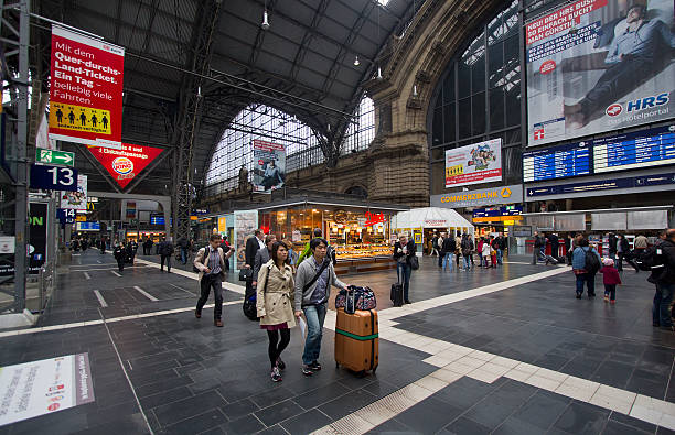 Frankfurt, Germany - April 30, 2014: Asian couple with suitcase and other train travelers walk among the kiosks in the central hall of Frankfurt railway station in Frankfurt, Germay on April 30, 2014