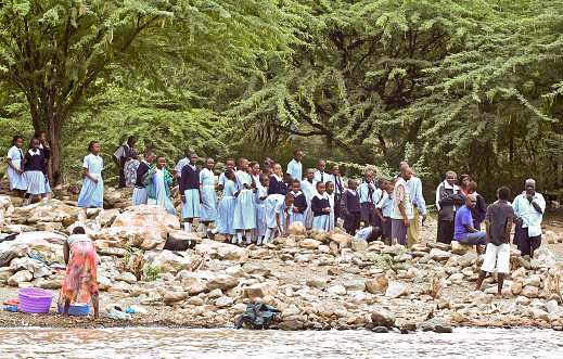 Baringo, Kenya - 28th July, 2006: A group of Kenyan school children in school uniform, with their teachers, waiting beside Lake Baringo, while a woman washes clothes at the edge of the lake.