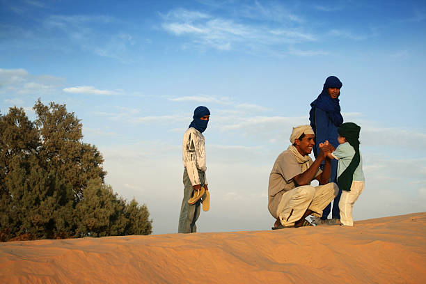 Golden hour on dune of Sahara Douz, Tunisia - September 22, 2007: Bedouins playing with little tourist on Sahara dune near Oasis Douz during golden hour, desert fox is between them tunisia sahara douz stock pictures, royalty-free photos & images