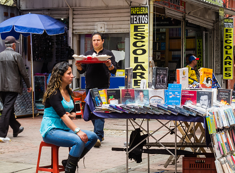 Bogota, Colombia - March 26, 2015: Street vendors on Calle or Street 16. This section of the street is closed to vehicular traffic and is an all pedestrian street.  The girl in the foreground is selling second-hand books.  Photo shot in the early afternoon sunlight; horizontal format.