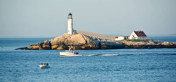 A speed boat speeds off in the distance with the light house watching over the calm waters, mountains caress the background on this hazy day on the river