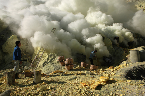 Kawah Ijen, Indonesia - August 9, 2011: Miner collects sulphur in the fumes of toxic volcanic gas at the sulphur mines in the crater of the active volcano of Kawah Ijen, East Java, Indonesia.