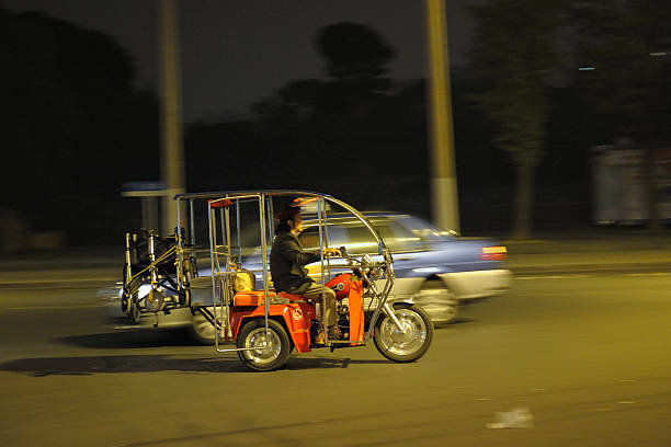 Shanghai, China - October 31, 2010: Disabled Chinese man on his tricycle transporting wheel-chair. Blur taxi in background. Night time. Panning, motion blur. Hight iso,grain