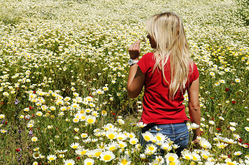 A young woman standing in a field of daisies.