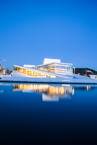 Oslo, Norway - April 21, 2015: View, at dusk, on the beautiful building of the Oslo Opera House. The white and modern structure is reflected on the deep blue see. The Oslo Opera House is the home of The Norwegian National Opera and Ballet, and the national opera theatre in Norway. 