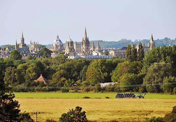 Oxford, UK - July 14, 2011:The skyline of the city of Oxford with foreground working farm and tractor collecting hay bales on agricultural land.