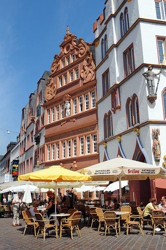 Trier, Germany - July 5, 2011: Tourists sitting in a Restaurant at Market place in Trier centre (Germany) enjoying the sun. Old houses from 17th century surrounding the place \