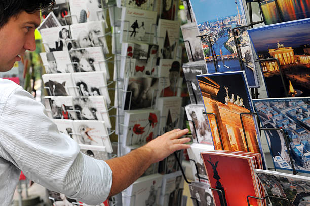 Berlin, Germany - August 3, 2011: young tourist in Kreuzberg looking at store for Berlin postcards. The postcard showing typical berlin sightseeing like Sony Center, Victory Column, Oberbaum Bridge.