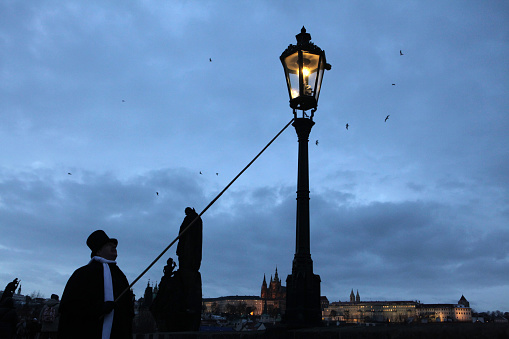 Prague, Czech Republic - December 10, 2012: Lamplighter lights a street gas light manually during the Advent at the Charles Bridge in Prague, Czech Republic. Street gas lights in the historical centre of Prague are lighted manually during the Advent only as a part of the Czech Christmas traditions.